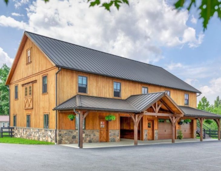 large renovated barn-style building with wooden siding, stone foundation, and a metal roof, surrounded by trees and a paved driveway