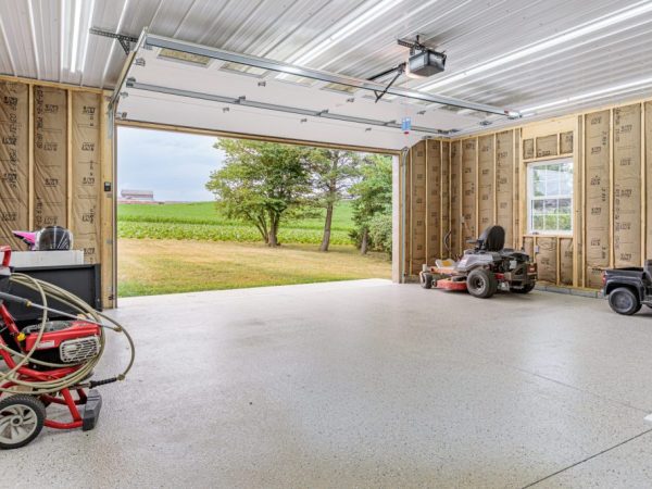 Interior view of a detached garage with exposed insulation, lawn equipment, and an open overhead door.