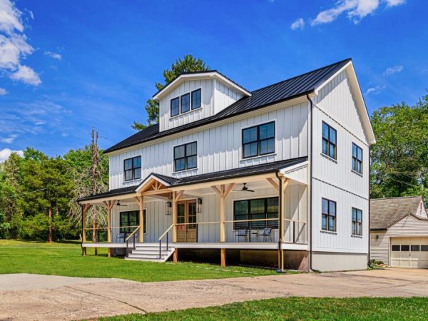 Front exterior of a white three-story home with black metal roof and front porch.
