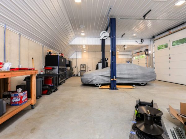 Interior of a garage workshop with a car lift, a covered vehicle, tool storage, and concrete floors.