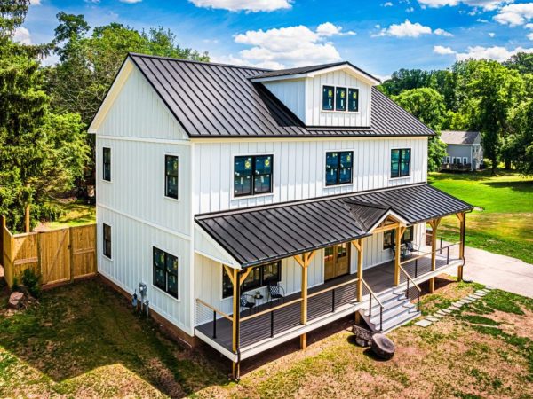 Side and front view of a white house with black standing seam roof and covered porch.