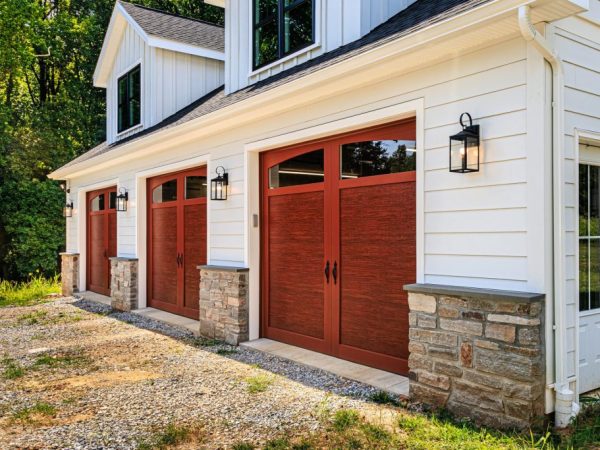Side angle of a white detached garage featuring faux wood garage doors, stone accents, and black exterior lights.
