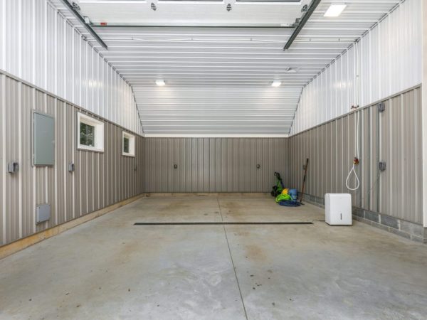 Empty garage bay with metal siding, high ceilings, concrete floor, and utility hookups along the walls.