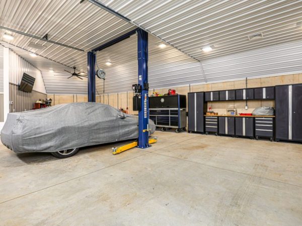 Interior view of a garage workshop showing a car lift, covered car, and a full wall of cabinets and tool storage.