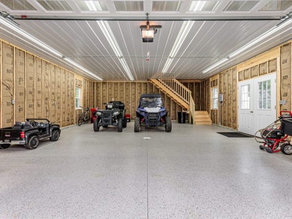 Interior of a detached garage showing insulation, ATVs, and a wooden staircase to a second floor.