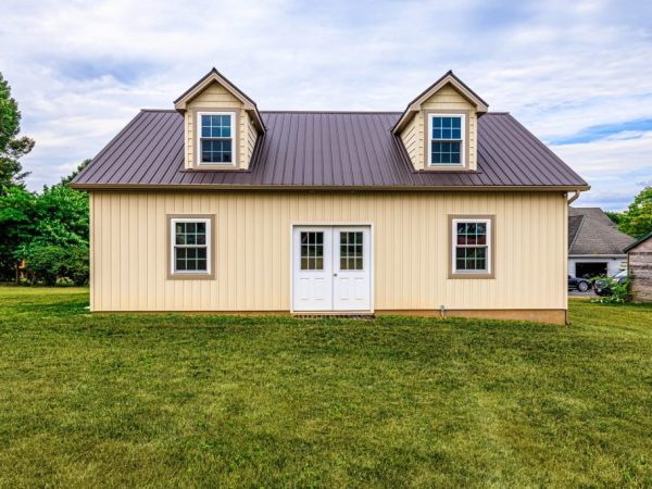 Rear view of a detached beige garage with two dormer windows and a white entry door.