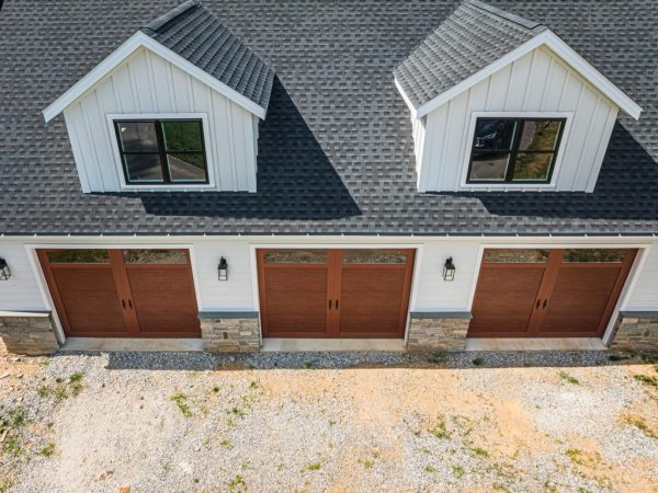 Aerial view of a large white detached garage with asphalt shingles, two dormers, and three matching garage doors.