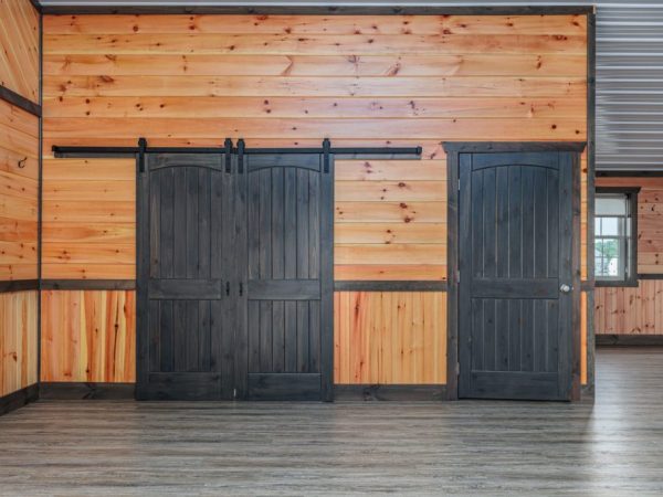 Interior view of double black sliding barn doors next to a single black door on a wood-paneled wall.