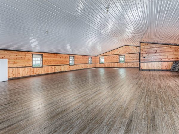 Spacious event room with vinyl plank flooring, pine wood walls, and arched metal ceiling.