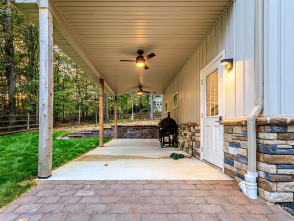 Close-up of a covered patio attached to a detached garage, featuring a grill, ceiling fans, and paver walkway.