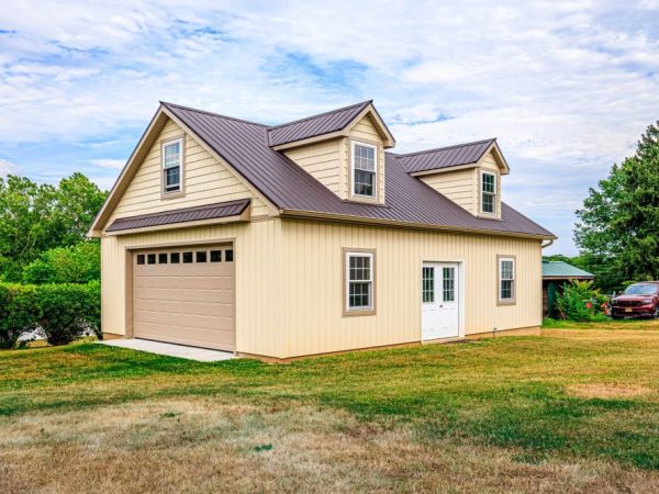 Angled view of a detached garage with cream siding, brown metal roof, and dormer windows