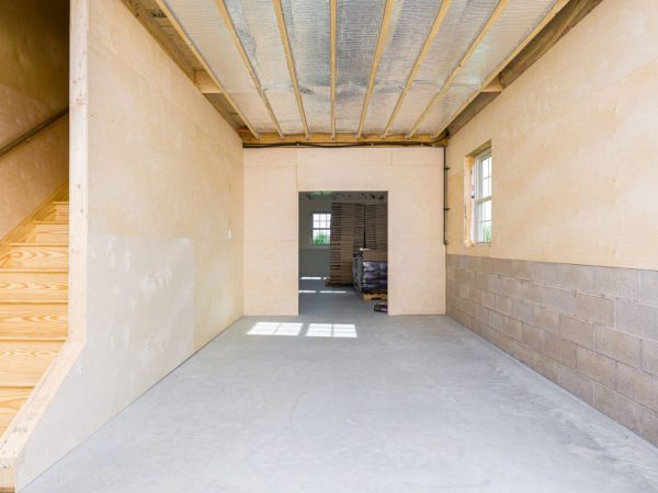 Unfinished garage interior with wood stairs, concrete floor, and open framed doorway leading to another room.