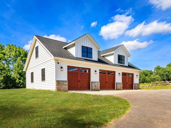 Angled front view of a white three-car garage with asphalt roof, stone accents, and matching dormers above each bay.