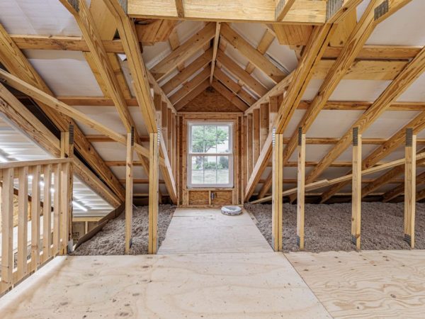 Unfinished second floor of a garage showing roof trusses, window, and plywood flooring