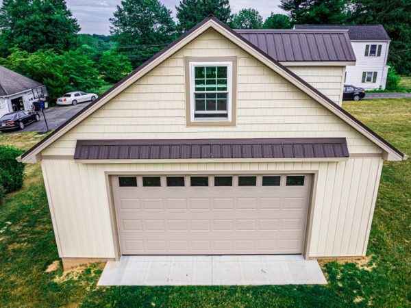 Front view of a cream-colored detached garage with a brown garage door and dormer window