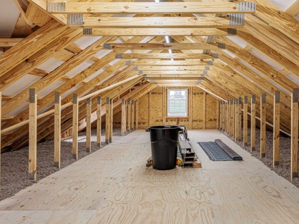 Unfinished attic space above a garage with plywood flooring and exposed roof trusses