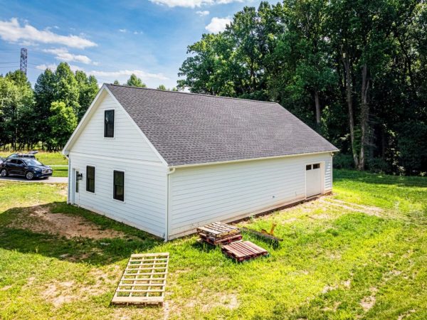 Rear view of a detached garage with white vinyl siding, black window frames, and a single rear entry door.