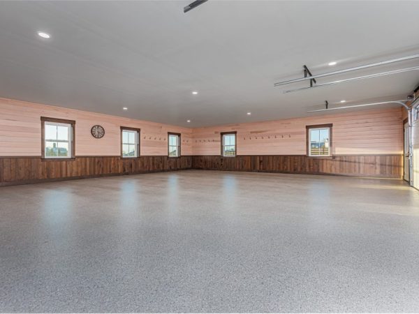 Spacious garage interior with wood-paneled walls, epoxy flooring, and multiple windows with natural light.