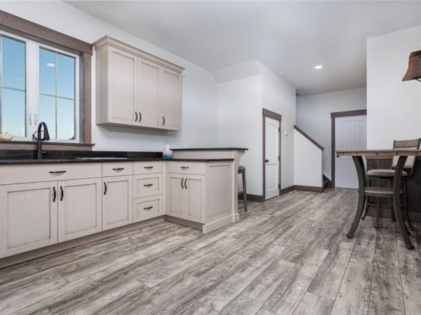 Modern kitchen with light cabinetry, dark countertops, and wood-look tile flooring in an apartment above a garage.