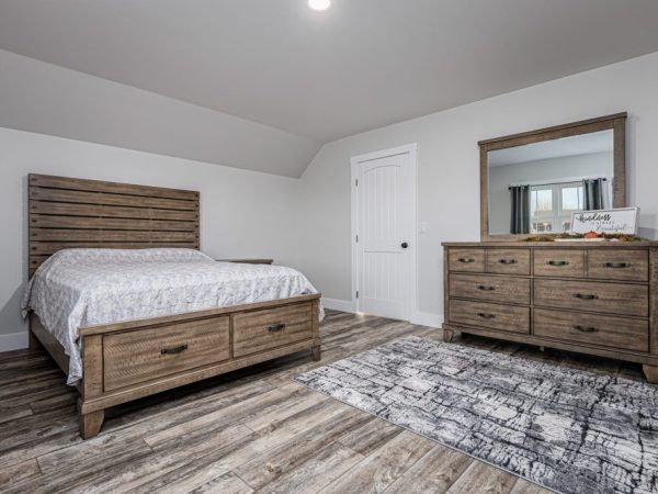 Bedroom with wooden bed frame, matching dresser and mirror, and rustic wood-style flooring.