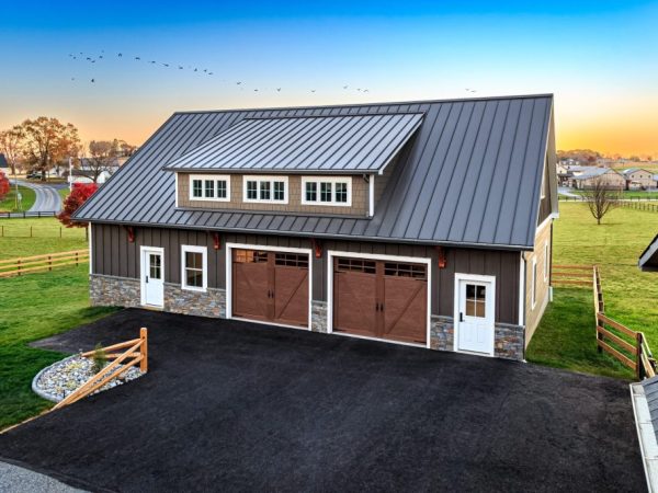 Detached two-car garage with stone wainscoting, wood-style doors, and a dormer window, set on a blacktop driveway.