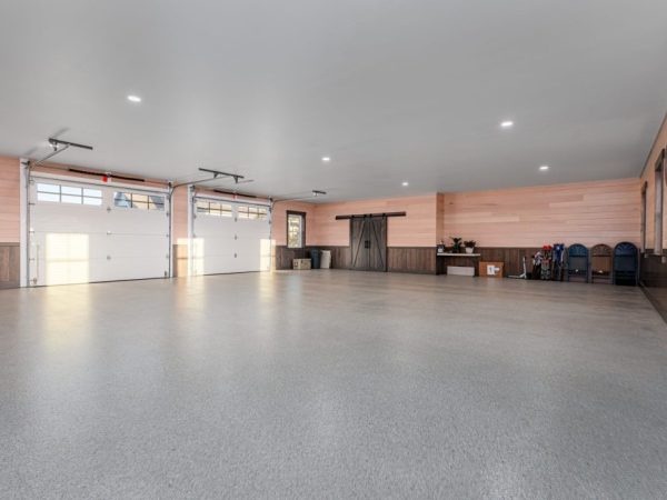 Large garage interior with barn doors, utility items, and windows letting in natural light, featuring finished walls.