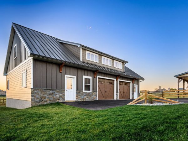 Two-car detached garage with stone base, brown doors, and vertical siding in a scenic rural setting.