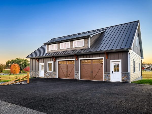 Two-car detached garage with brown siding, stone accents, wood-style garage doors, and a black metal roof.