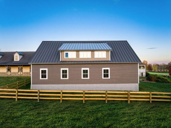 Rear view of detached garage with five white windows, tan siding, and a large dormer, enclosed by a wooden fence.