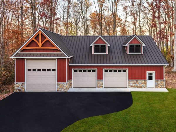 Front view of red garage with black metal roof, dormer windows, and three overhead doors, set against a wooded backdrop.