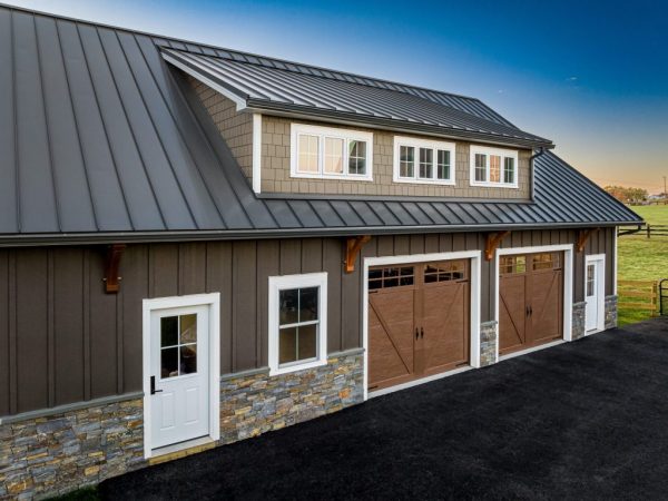 Close-up of two-car garage with stone wainscoting, brown vertical siding, and wood-style garage doors beneath dormer windows.
