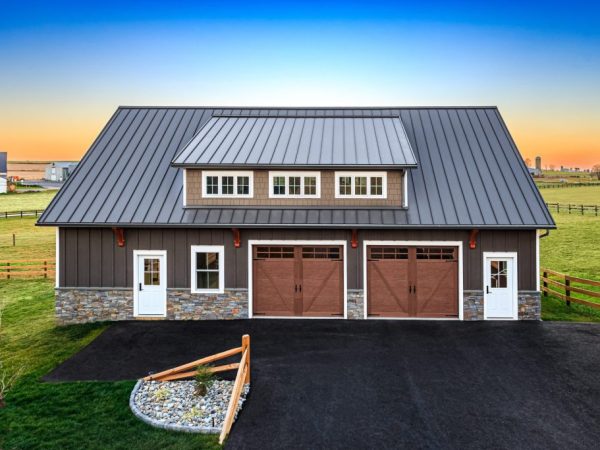 Front view of newly built detached garage with stone base, two garage doors, and two entry doors at sunset.