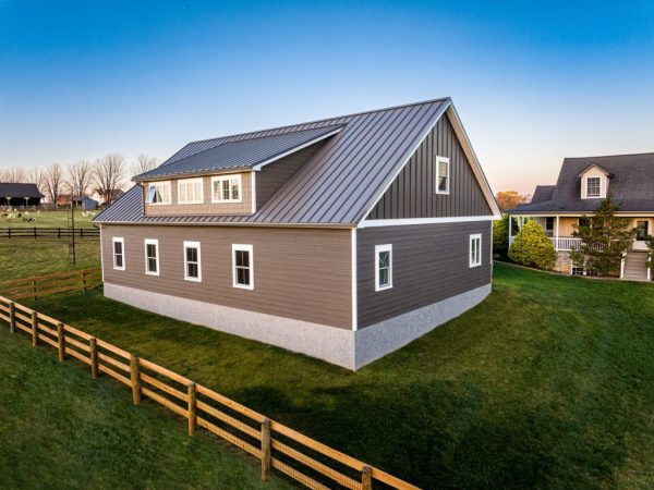 Angled rear view of detached garage with brown and gray siding, multiple windows, and a metal roof, set in a grassy yard.