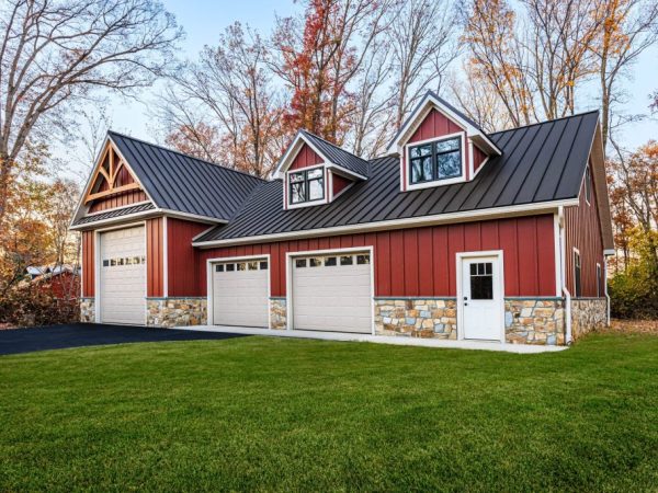 Red and stone garage with three overhead doors, black metal roof, and side entrance door, surrounded by grass and trees.