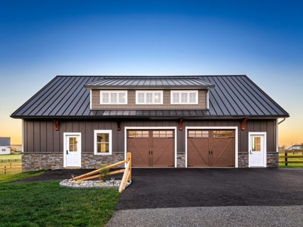 Front view of luxury two-car garage with dormer windows, stone and vertical siding, and carriage-style garage doors.