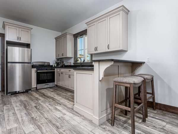 Compact kitchen with cream-colored cabinets, dark countertops, stainless steel appliances, and breakfast bar in a garage apartment.
