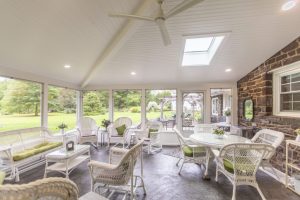 bright three season room with white ceilings, wicker furniture, and full screen windows overlooking a green lawn. 