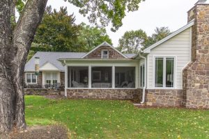 back view of a house with a stone and white siding sunroom addition featuring full screen panels and large windows