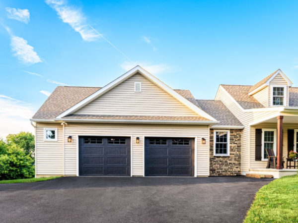 front facing view of a two car garage with dark carriage-style doors on beige vinyl home
