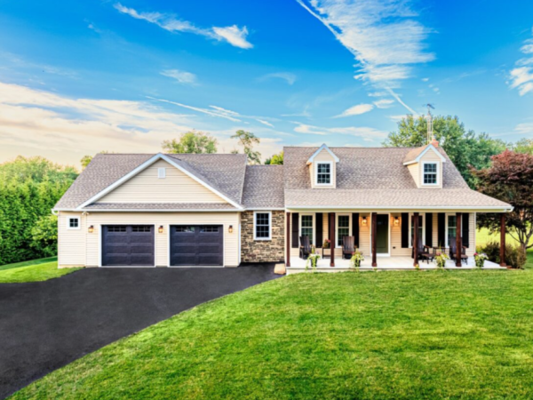 wide shot of home with dormers, stone accents, large front lawn, and attached two car garage
