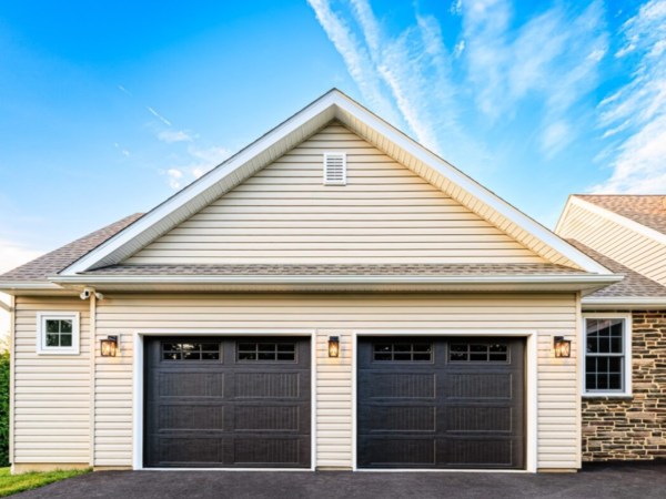 straight on view of two dark carriage style garage doors with tan siding and stone accents