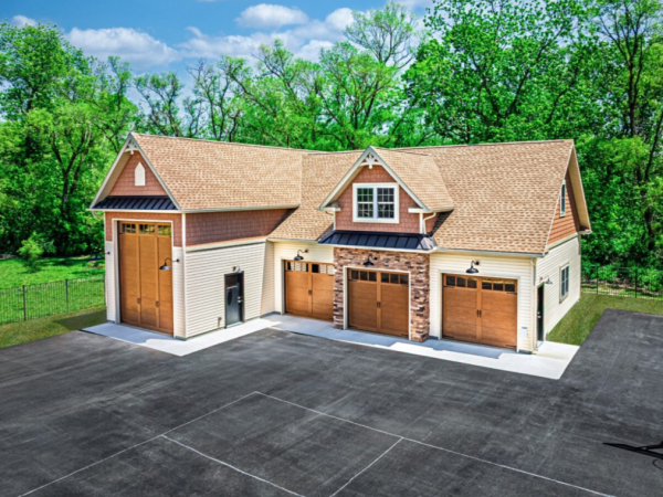 wide view of a custom garage with three standard doors and one tall RV-sized door, tan siding, and stone accents