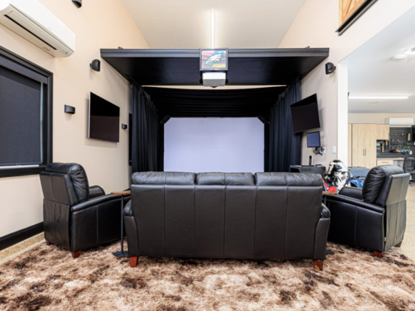 home golf simulator lounge featuring black leather seating, shaggy carpet, and dual TVs