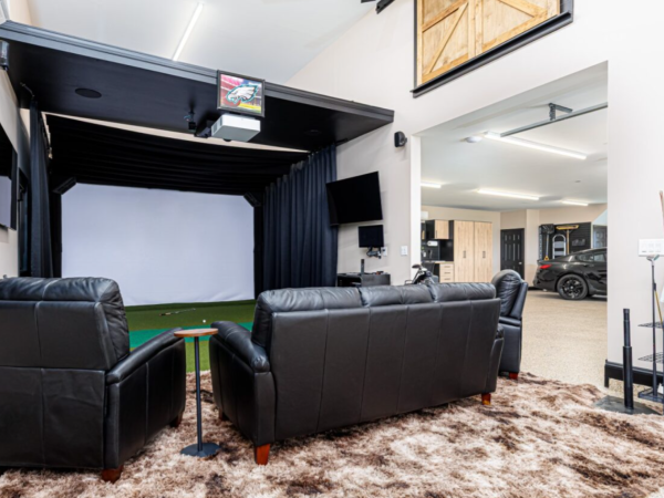 indoor golf simulator setup with lounge chairs, projectors, and garage access in the background