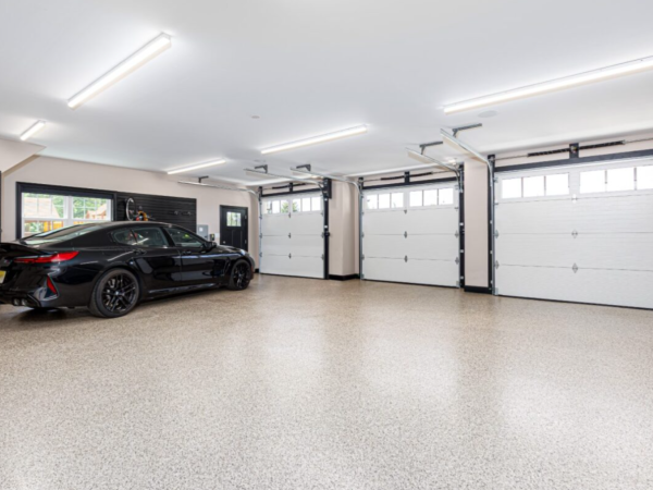 open view of garage with epoxy floor, black car, and three white overhead garage doors